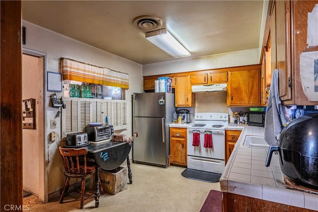 kitchen featuring white electric range, tile counters, and stainless steel refrigerator