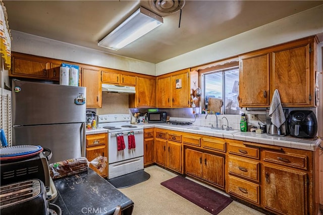 kitchen featuring tile counters, sink, white electric range, and stainless steel refrigerator