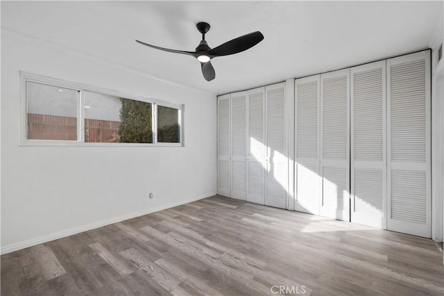 unfurnished bedroom with ceiling fan, light wood-type flooring, and two closets