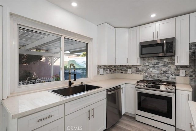 kitchen with backsplash, sink, light wood-type flooring, stainless steel appliances, and white cabinets