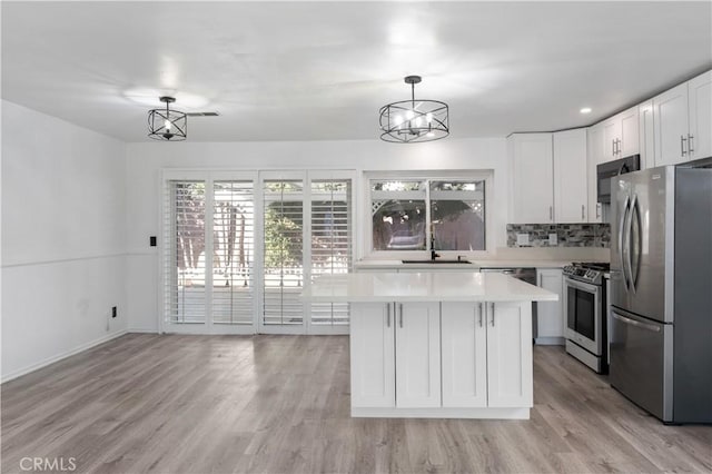 kitchen with stainless steel appliances, backsplash, decorative light fixtures, a kitchen island, and white cabinets