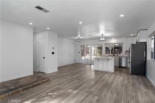 kitchen featuring white cabinets, a center island, decorative light fixtures, stainless steel appliances, and light wood-type flooring