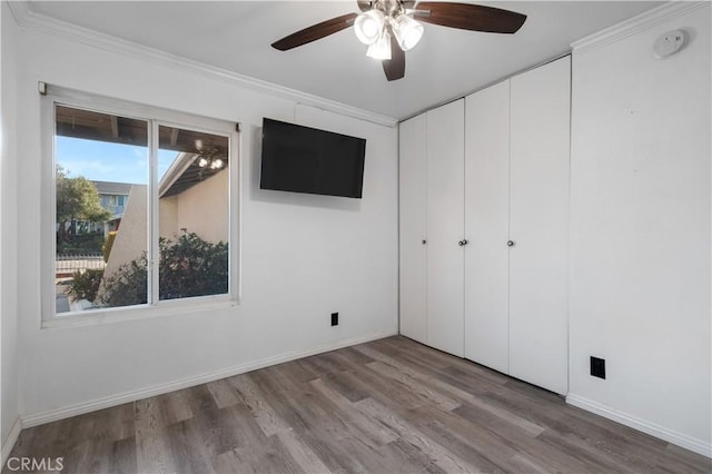 unfurnished bedroom featuring ceiling fan, wood-type flooring, a closet, and ornamental molding