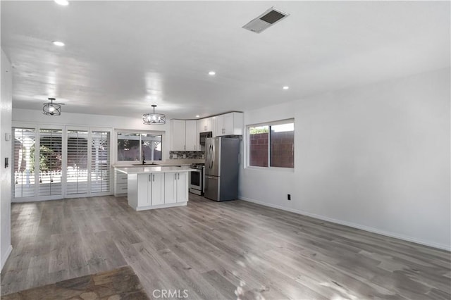 kitchen featuring white cabinets, a center island, decorative light fixtures, stainless steel appliances, and light wood-type flooring