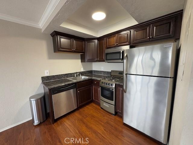 kitchen featuring dark wood-style flooring, stainless steel appliances, dark countertops, ornamental molding, and dark brown cabinets