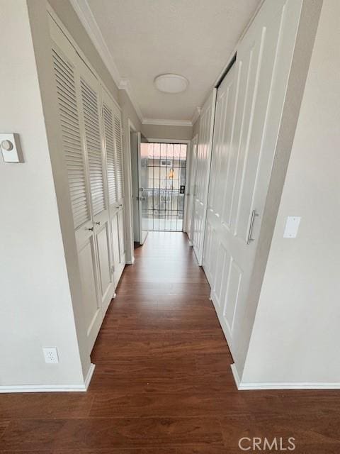 corridor with ornamental molding, dark wood-type flooring, and baseboards