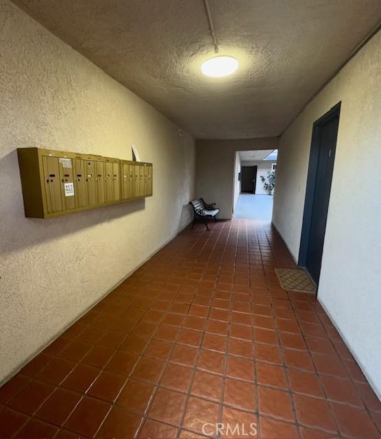 hall featuring tile patterned floors, mail area, a textured ceiling, and a textured wall