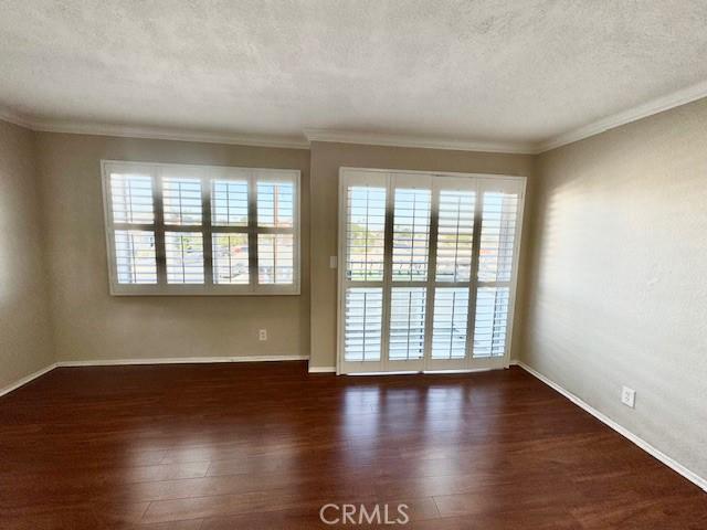 unfurnished room featuring a textured ceiling, plenty of natural light, wood finished floors, and crown molding