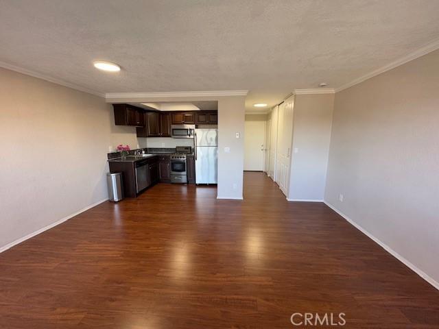 kitchen featuring dark countertops, dark wood-style flooring, stainless steel appliances, crown molding, and dark brown cabinets