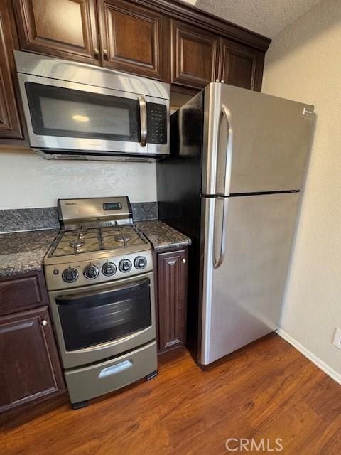 kitchen with dark wood-style floors, appliances with stainless steel finishes, dark countertops, and dark brown cabinetry