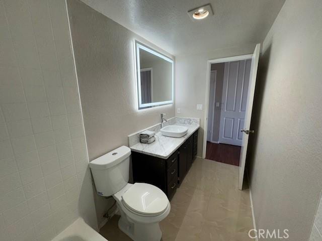 full bathroom featuring a textured wall, vanity, and toilet