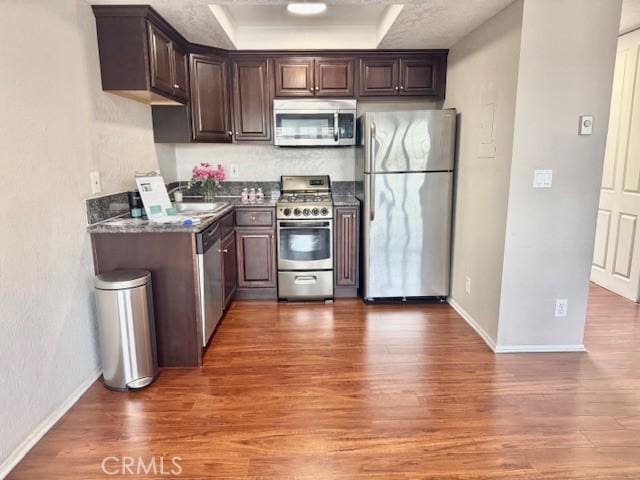 785 W 19th St Unit 12B, San Pedro, CA 90731 - kitchen featuring stainless steel appliances, wood finished floors, a tray ceiling, dark brown cabinetry, and dark stone countertops