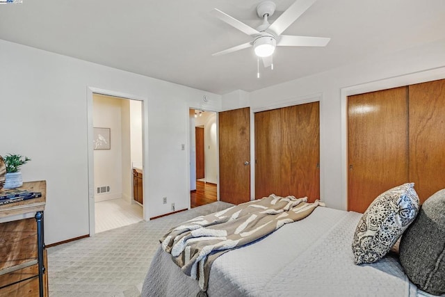 bedroom with ceiling fan, ensuite bath, multiple closets, and carpet flooring