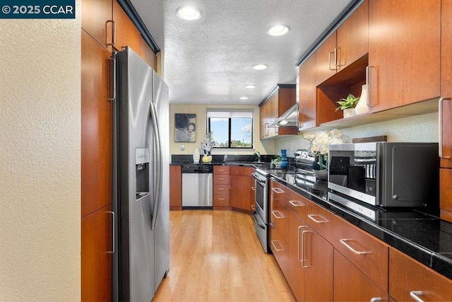 kitchen featuring sink, extractor fan, a textured ceiling, light hardwood / wood-style flooring, and appliances with stainless steel finishes