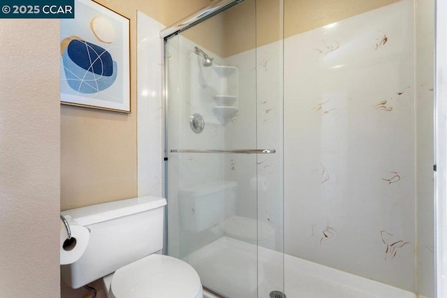 bathroom featuring a shower with shower door and toilet