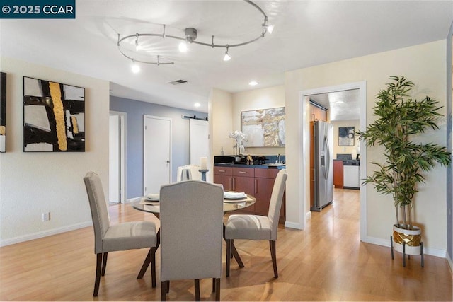 dining space with track lighting, light hardwood / wood-style floors, and a barn door