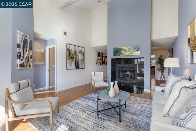 living room with a tile fireplace, wood-type flooring, and a towering ceiling