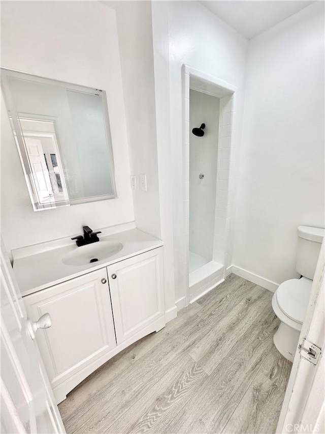 bathroom featuring hardwood / wood-style flooring, vanity, toilet, and a tile shower