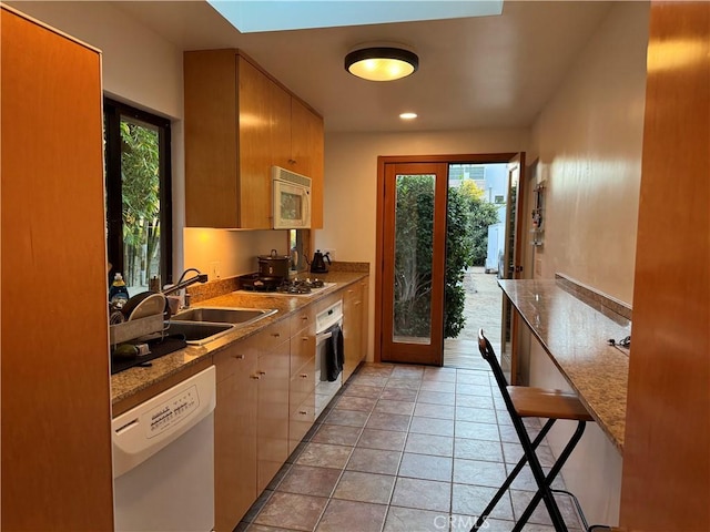 kitchen with white appliances, sink, a kitchen breakfast bar, light tile patterned flooring, and light stone counters