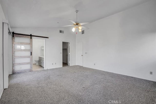 unfurnished bedroom featuring ensuite bathroom, a barn door, ceiling fan, vaulted ceiling, and light carpet