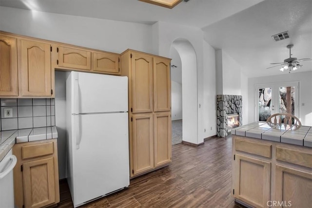 kitchen featuring ceiling fan, decorative backsplash, light brown cabinets, tile counters, and white refrigerator