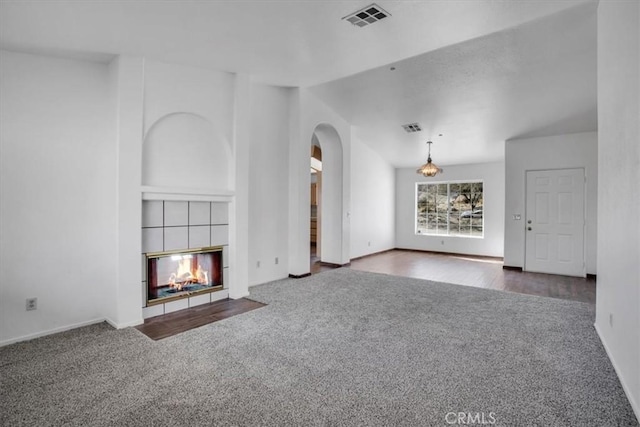 unfurnished living room with dark carpet, a tile fireplace, and lofted ceiling