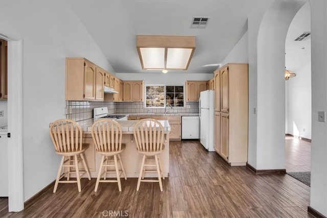 kitchen with kitchen peninsula, white appliances, light brown cabinets, a breakfast bar area, and dark hardwood / wood-style flooring