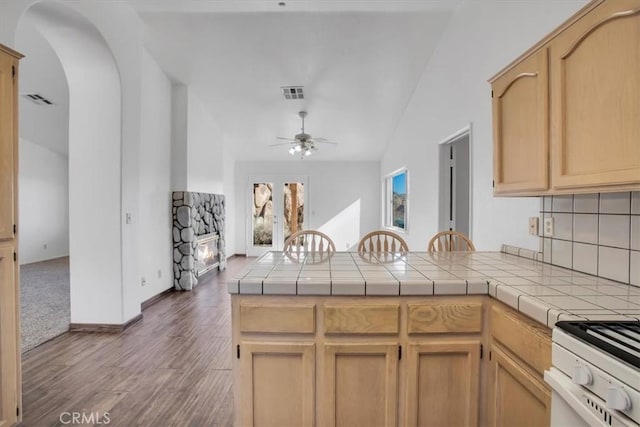 kitchen featuring tile counters, a fireplace, light brown cabinetry, kitchen peninsula, and ceiling fan