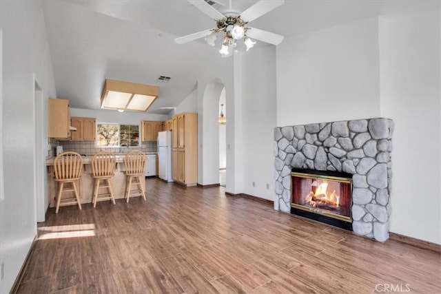 living room featuring ceiling fan, hardwood / wood-style flooring, lofted ceiling, and a stone fireplace