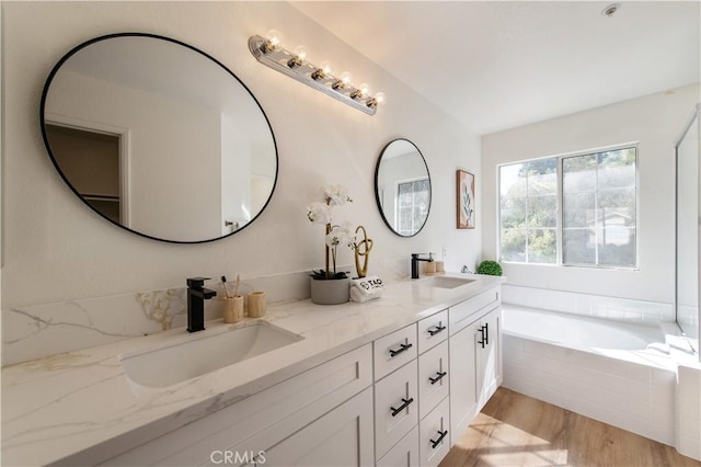 bathroom featuring a relaxing tiled tub, wood-type flooring, and vanity