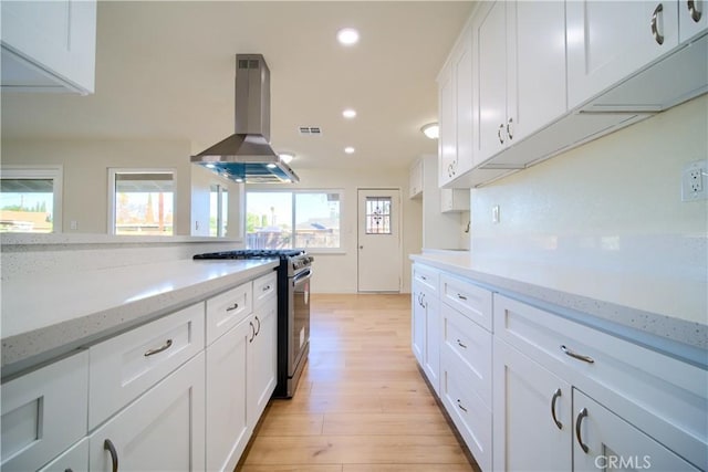 kitchen featuring stainless steel range with gas cooktop, white cabinets, island exhaust hood, light stone counters, and light hardwood / wood-style flooring