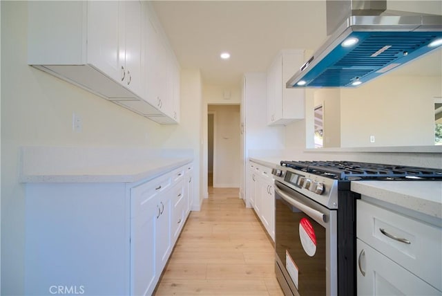 kitchen featuring island range hood, stainless steel range with gas stovetop, light hardwood / wood-style floors, and white cabinets