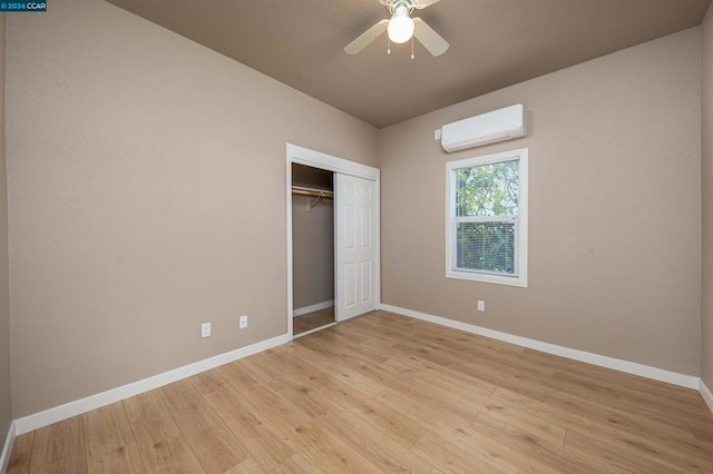 unfurnished bedroom featuring ceiling fan, a wall mounted AC, light hardwood / wood-style flooring, and a closet