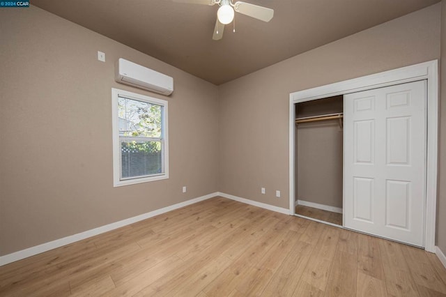 unfurnished bedroom featuring an AC wall unit, a closet, ceiling fan, and light wood-type flooring