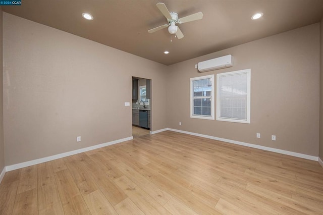 unfurnished room with light wood-type flooring, ceiling fan, sink, and a wall mounted air conditioner