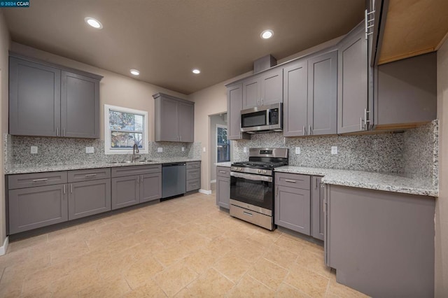 kitchen with appliances with stainless steel finishes, sink, gray cabinetry, and light stone counters