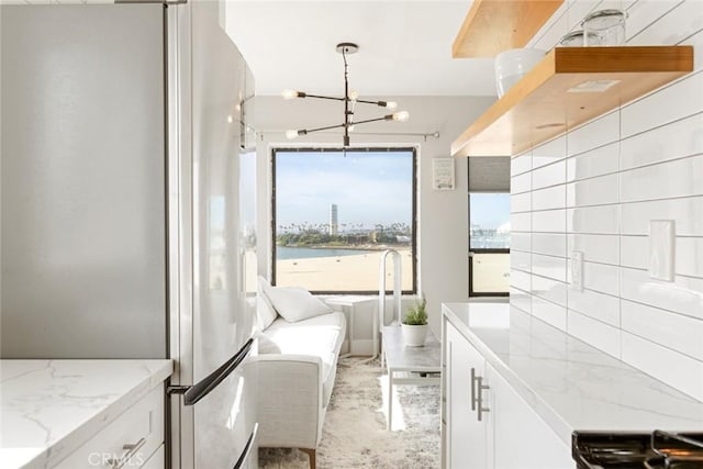 kitchen with decorative light fixtures, a notable chandelier, white cabinetry, light stone countertops, and stainless steel fridge