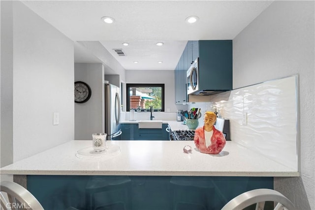 kitchen with a peninsula, a sink, visible vents, appliances with stainless steel finishes, and blue cabinetry