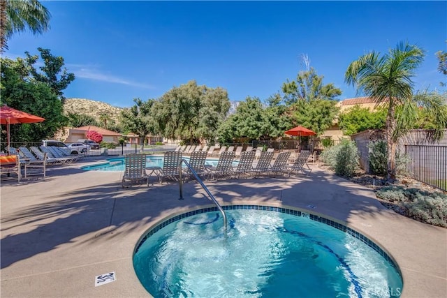 community pool with a patio area, a hot tub, fence, and a mountain view