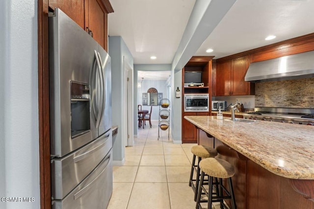 kitchen with sink, stainless steel appliances, light tile patterned floors, wall chimney exhaust hood, and light stone counters