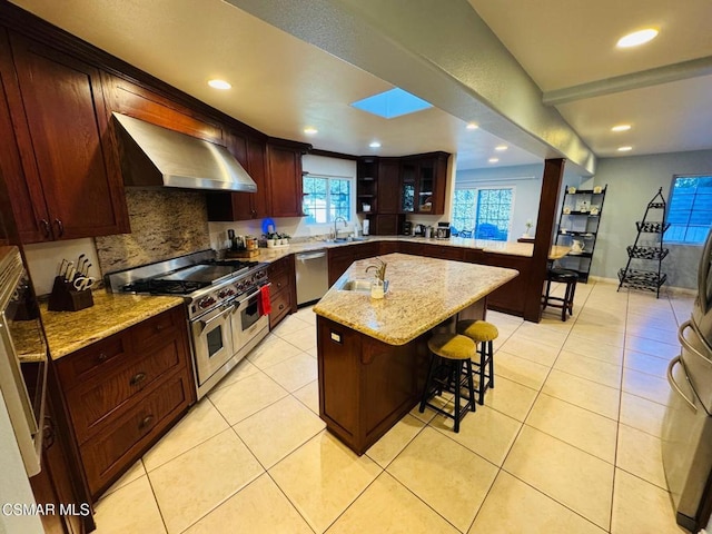 kitchen with a center island, wall chimney range hood, stainless steel appliances, sink, and a breakfast bar