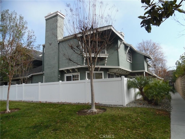 back of property with a chimney, fence, and a lawn