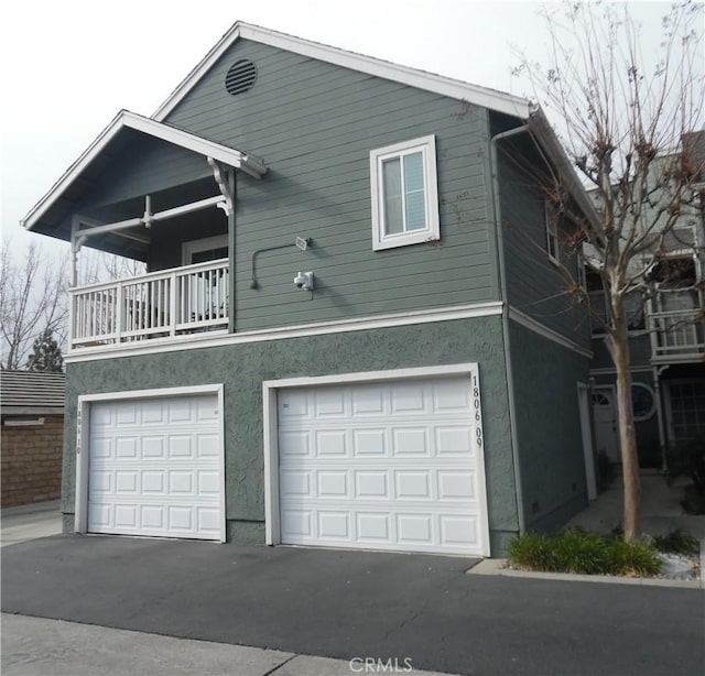 exterior space featuring a garage, a balcony, and stucco siding