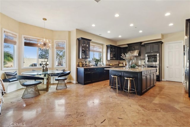 kitchen with a kitchen bar, light stone counters, a center island, hanging light fixtures, and double oven