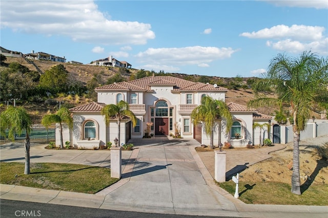 mediterranean / spanish-style house featuring a balcony, fence, concrete driveway, and stucco siding