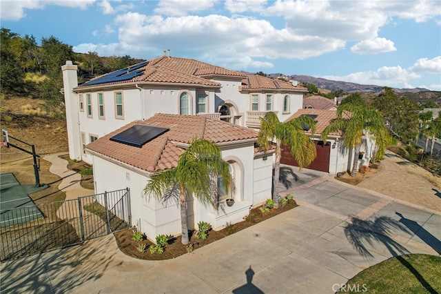 mediterranean / spanish-style home with a tile roof, solar panels, stucco siding, fence, and driveway