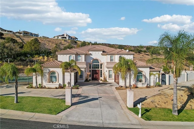 mediterranean / spanish house featuring stucco siding, driveway, a balcony, and fence