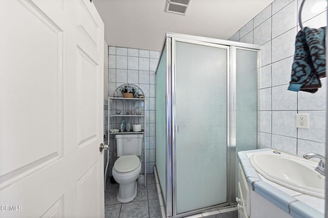 bathroom with toilet, tile patterned flooring, tile walls, and a shower with shower door