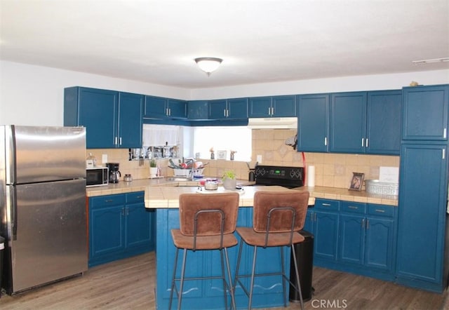 kitchen featuring tasteful backsplash, appliances with stainless steel finishes, blue cabinetry, and dark wood-type flooring