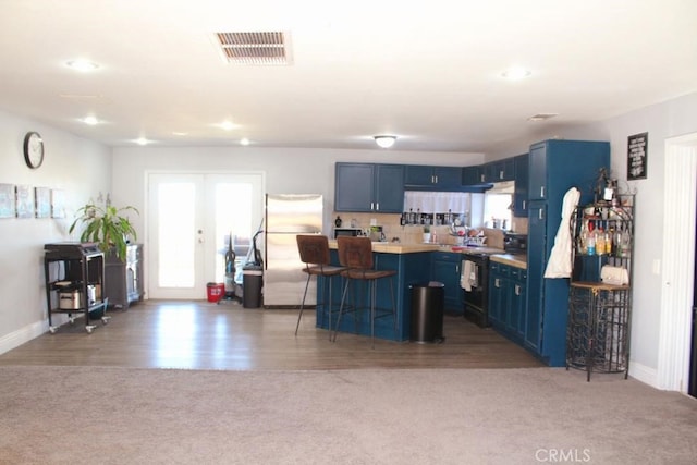 kitchen featuring blue cabinets, black electric range oven, a breakfast bar area, and stainless steel built in fridge